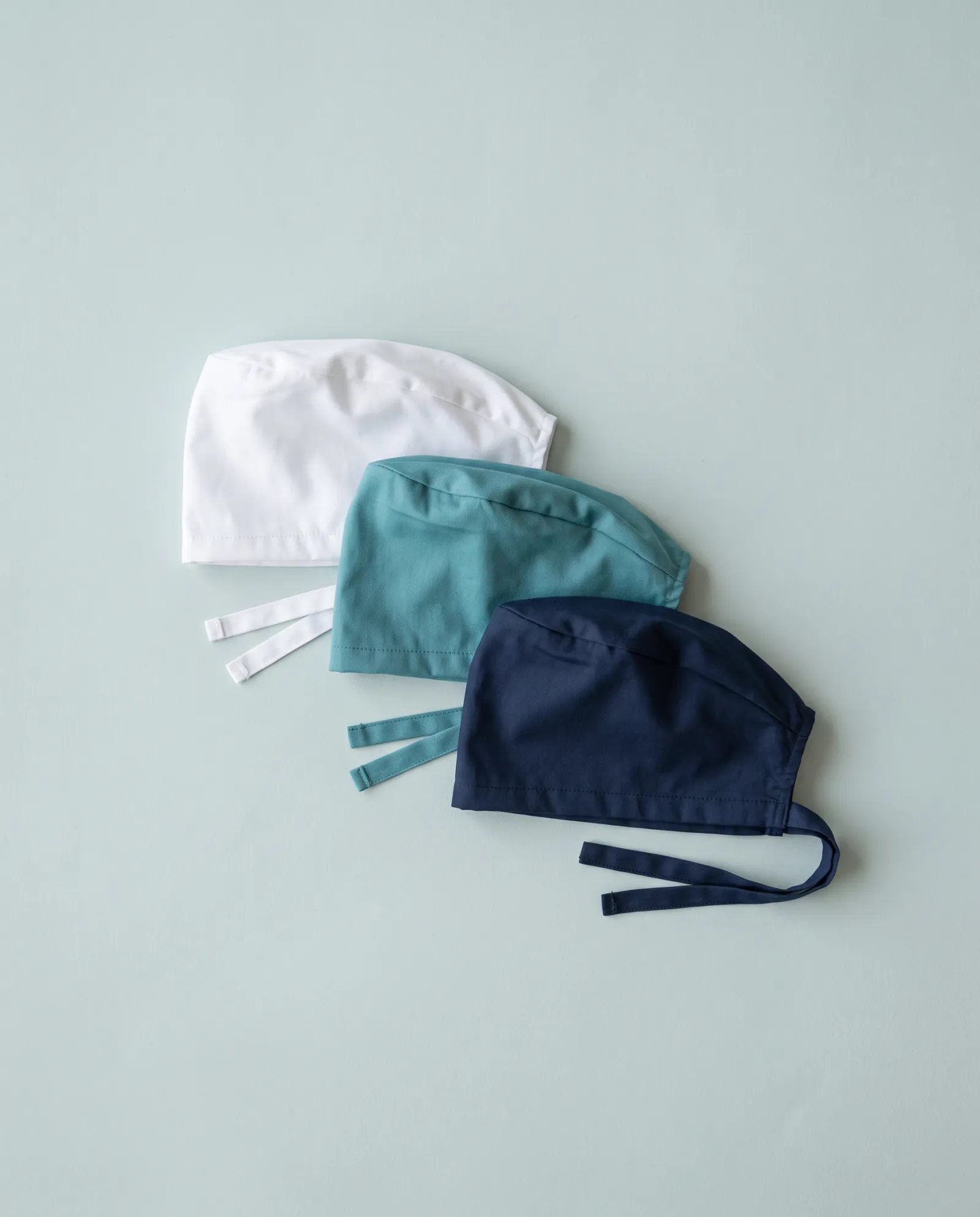 Tres gorros quirúrgicos doblados en blanco, turquesa y marino
